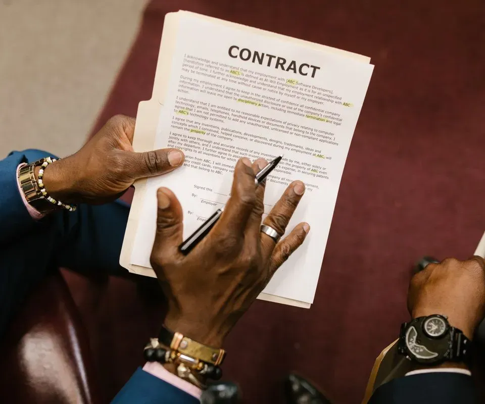 Hands holding a contract and a pen across a desk