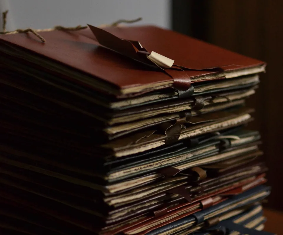 A tall stack of old folders tied with ribbons on a wooden desk