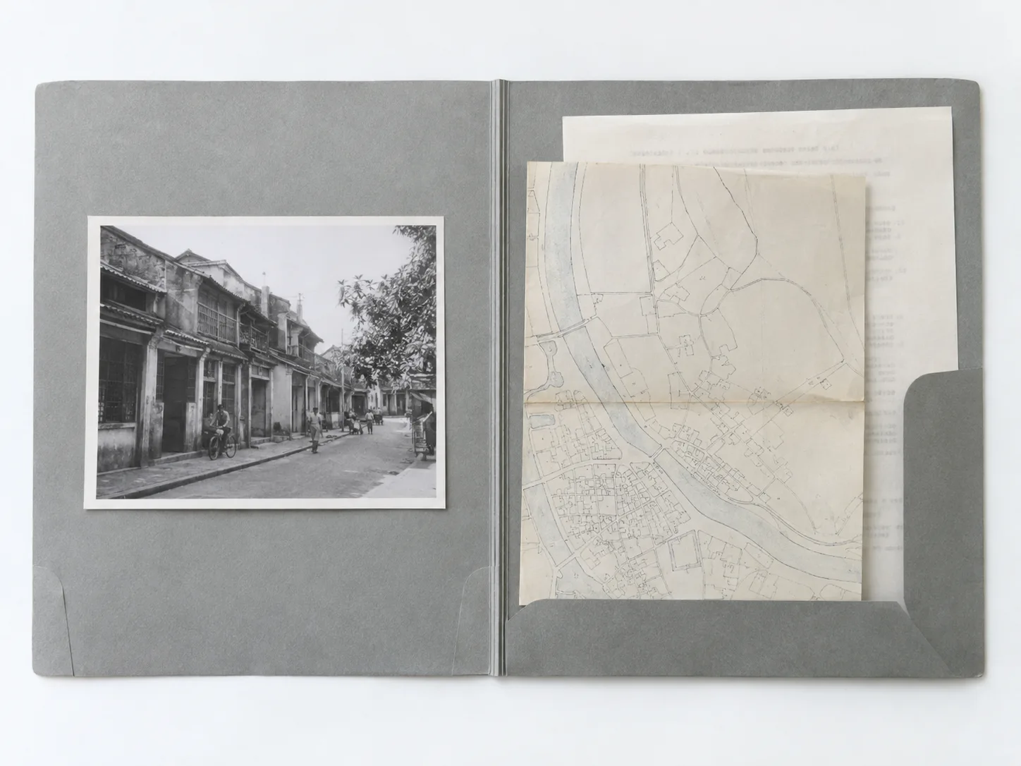An open grey file folder holding an old street photo and a folded map