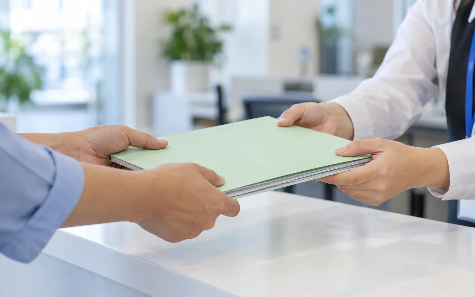 At a one-stop counter, two hands pass a pale green file folder