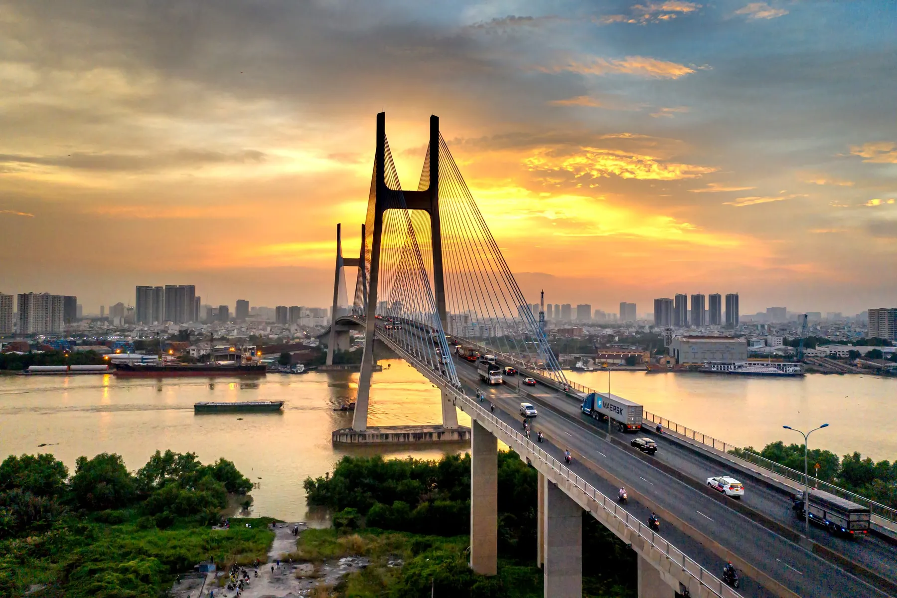 A cable-stayed bridge with two towers over a river at sunset, the city behind it
