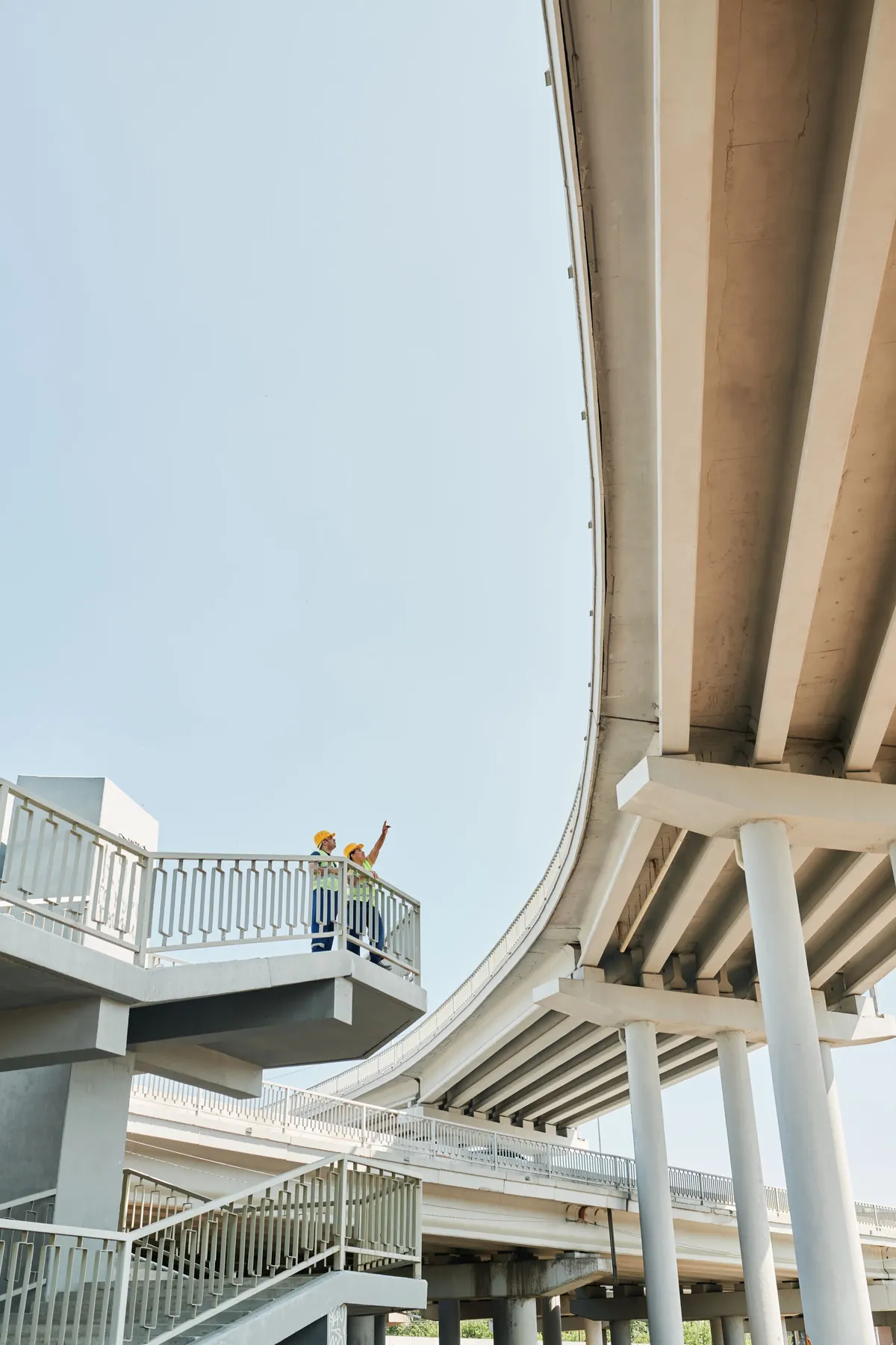 Two engineers in hard hats checking a concrete overpass from a walkway