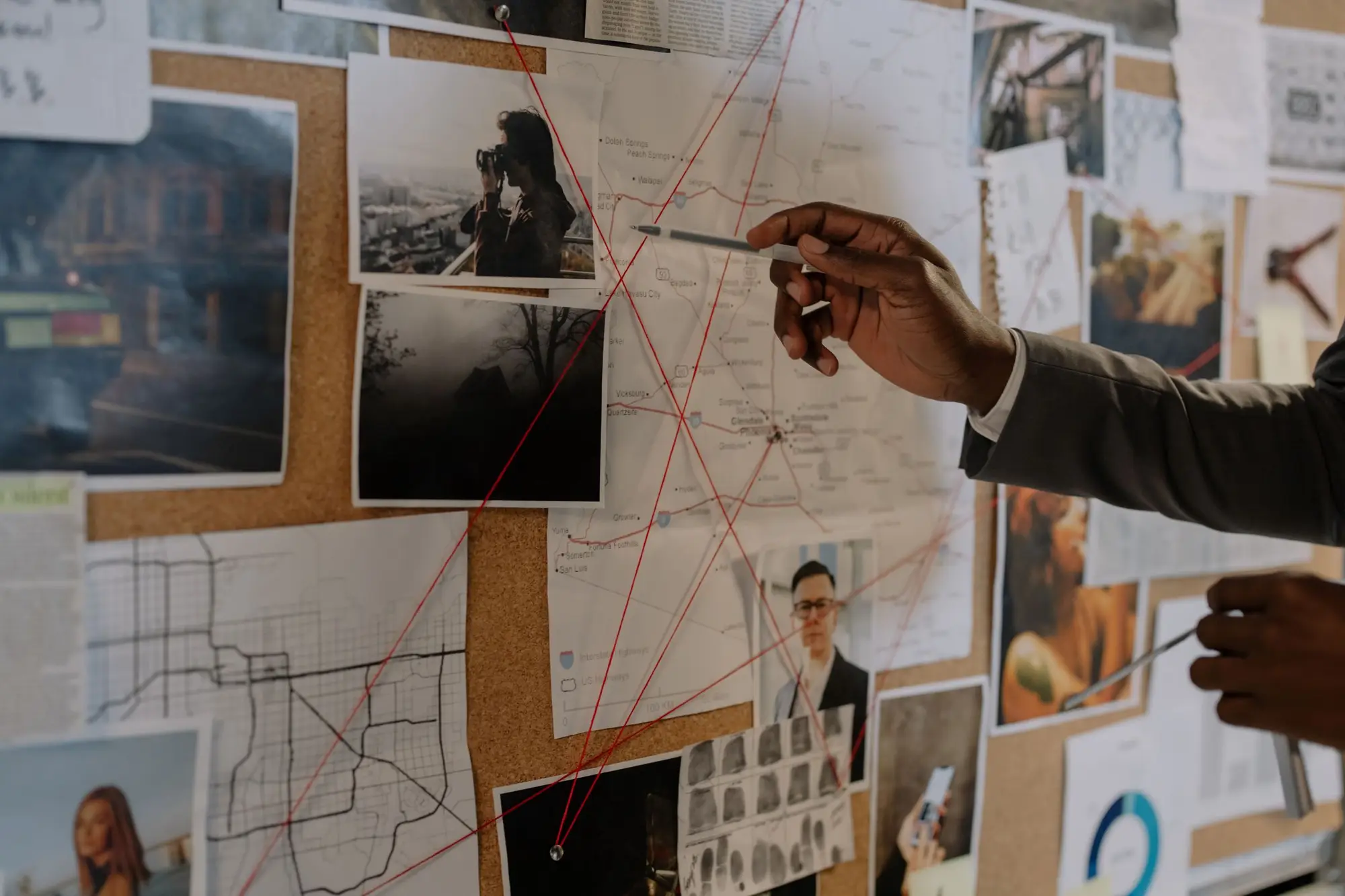 A hand with a pen pointing at notes and photos pinned on a board