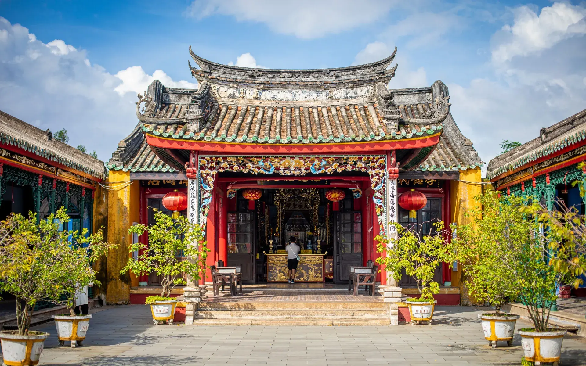 The gate of an old temple in Hoi An, with a curved tiled roof and red lanterns